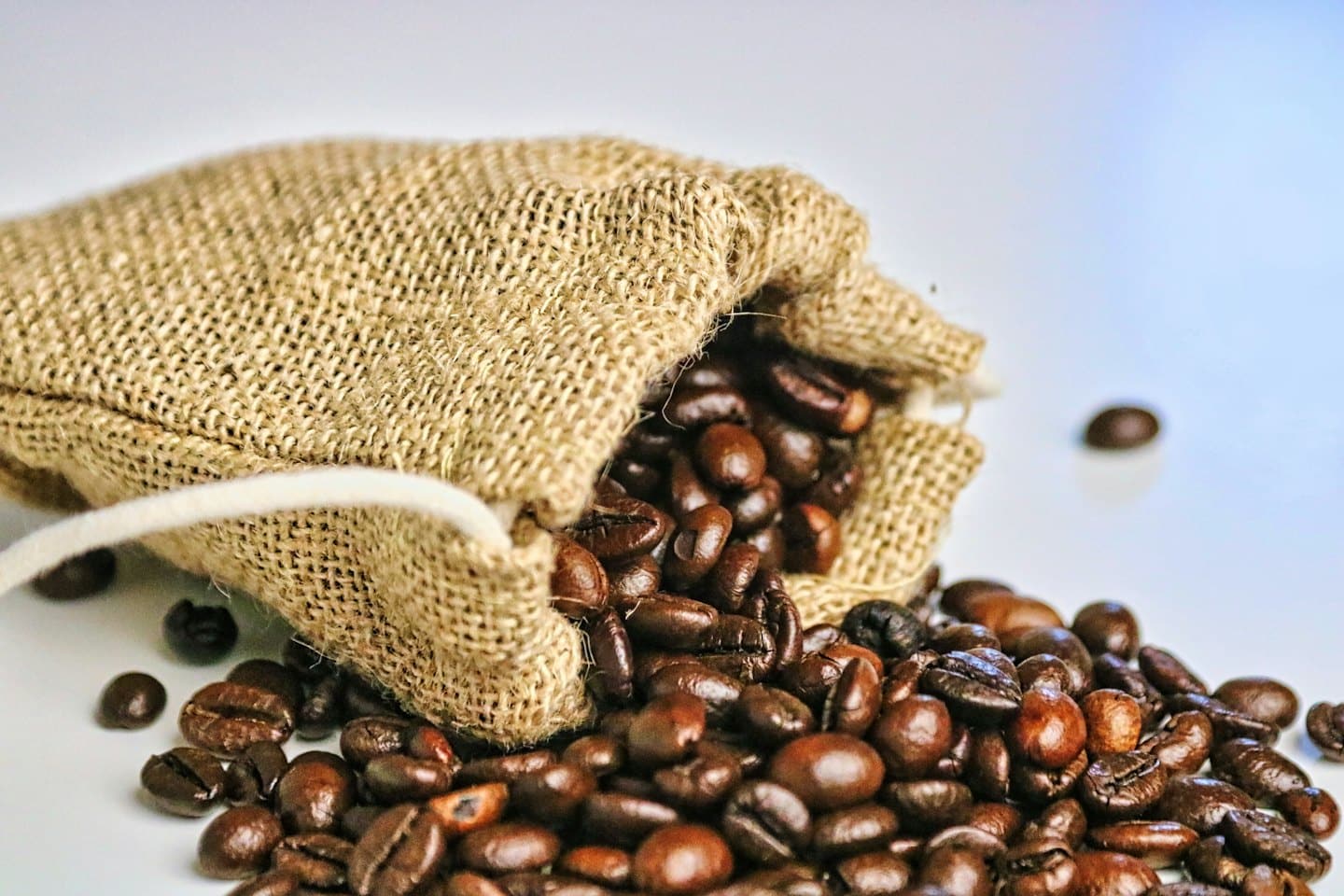 Dark roasted coffee beans spill from a textured burlap sack.